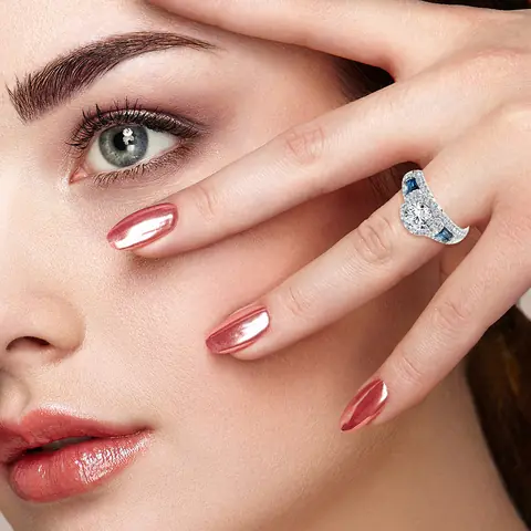A diamond halo engagement ring with blue baguette side stones worn on a hand held to a woman's face