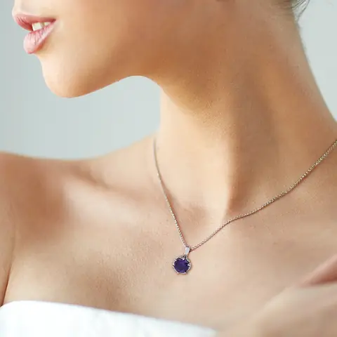 A round amethyst pendant in a scalloped white-gold setting on a fine chain, worn at the collarbone