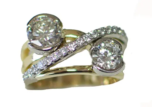 A two-stone diamond ring in yellow and white gold: two round diamonds in curved bezels, joined by a sweeping band of small diamonds